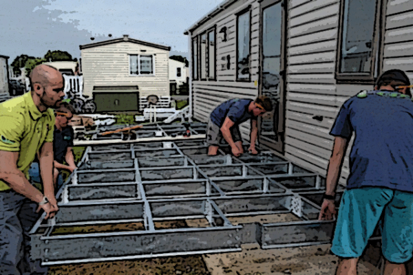 Men installing steel subframe against a caravan