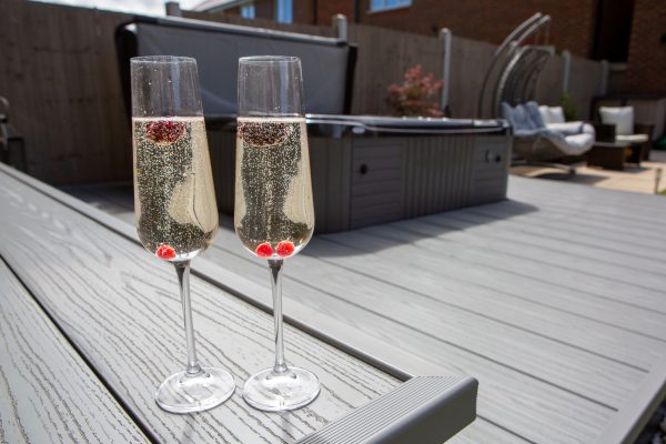 2 champagne glasses on light grey deck next to the hottub