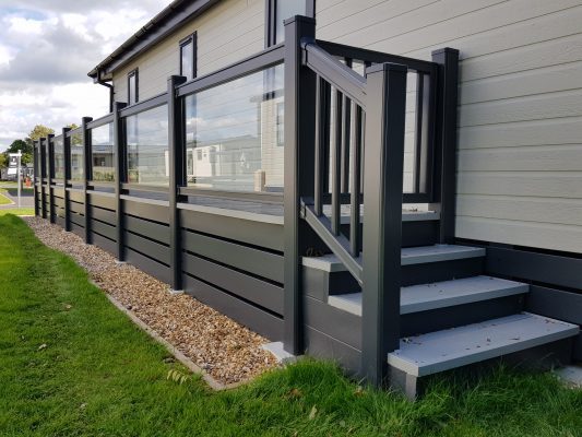 glass walkway with dark grey decking posts and caravan plinth